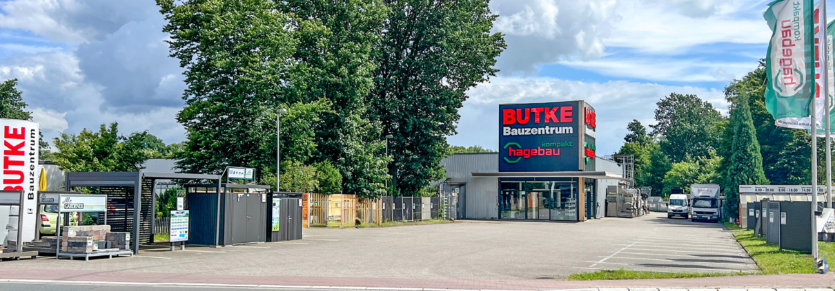 Aufnahme des Baumarkts von der Straße aus. Im Zentrum der Eingangsbereich mit den Logos Butke Bauzentrum und Hagebau kompakt