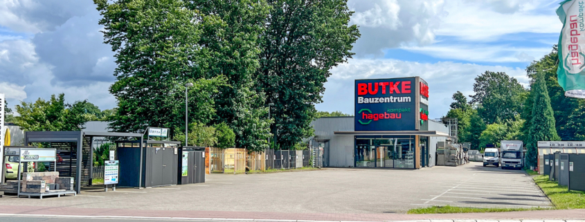 Aufnahme des Baumarkts von der Straße aus. Im Zentrum der Eingangsbereich mit den Logos Butke Bauzentrum und Hagebau kompakt